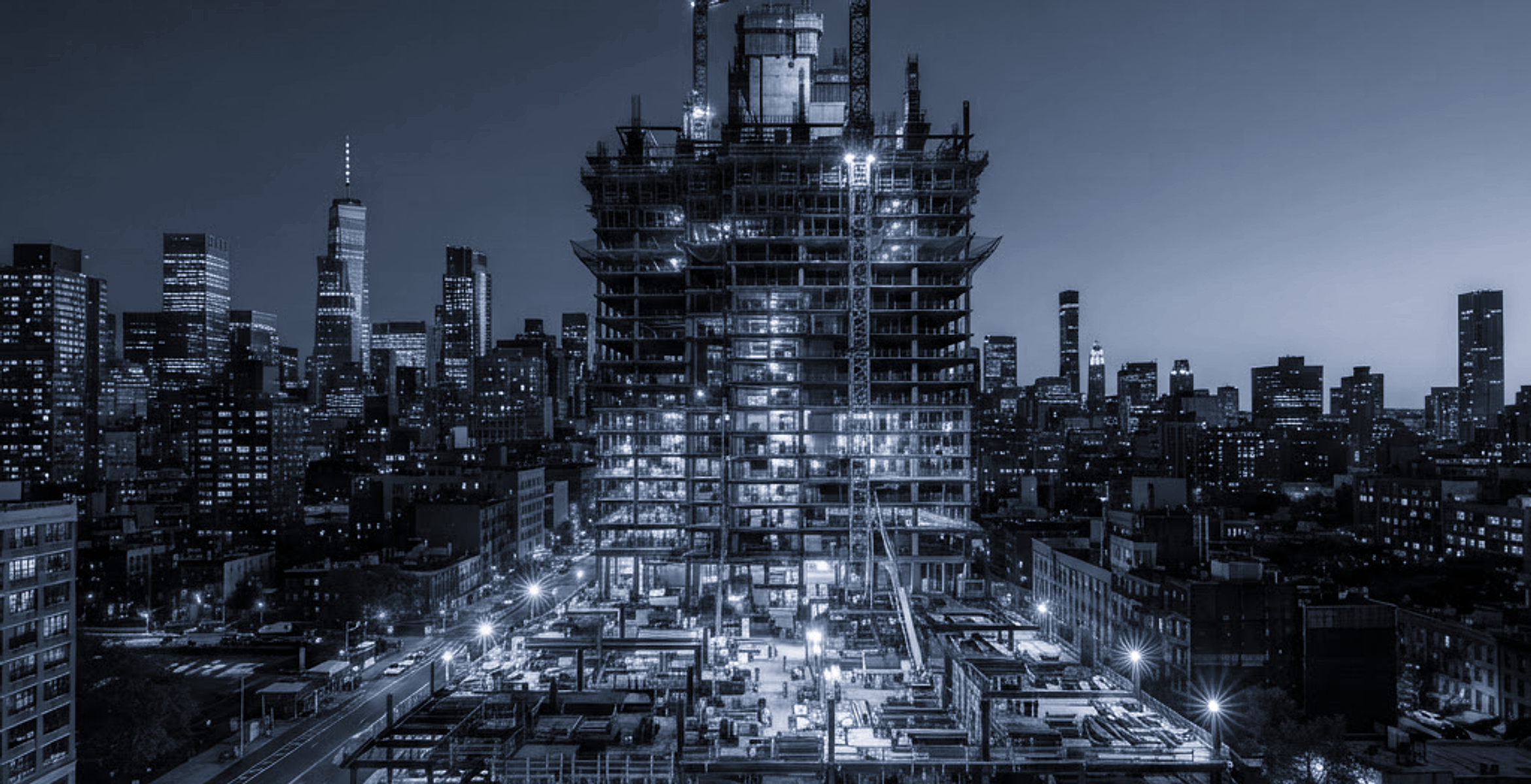 Active high-rise construction site with tower cranes and exposed steel framing at dusk